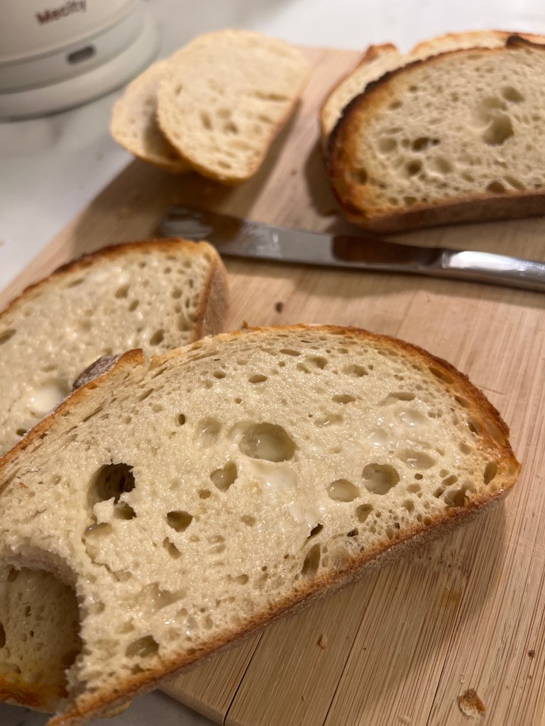 Costco’s Rustic Italian Bread loaf on a wooden board, sliced to show its thick crust and dense crumb.”